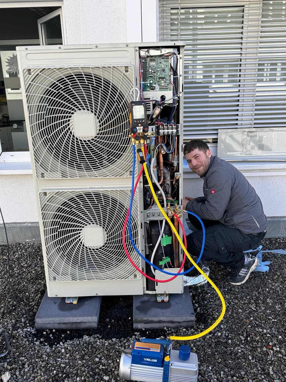 Techniker prüft ein geöffnetes Außengerät mit Manometerbatterie und Vakuumpumpe.