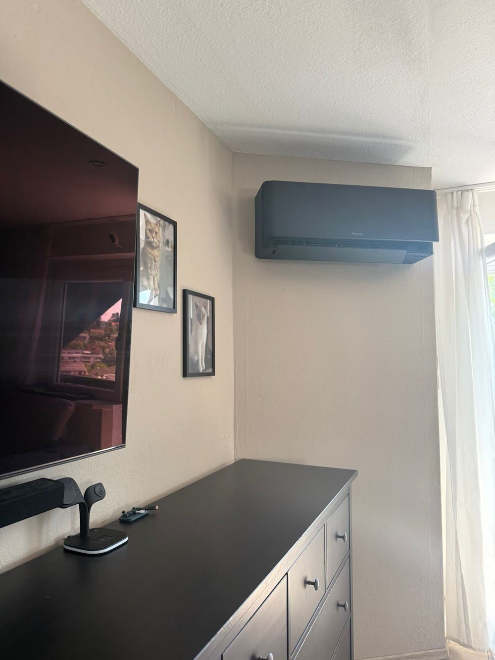 Klimagerät an einer Wand über einer Kommode mit Fernseher in einem Wohnraum.